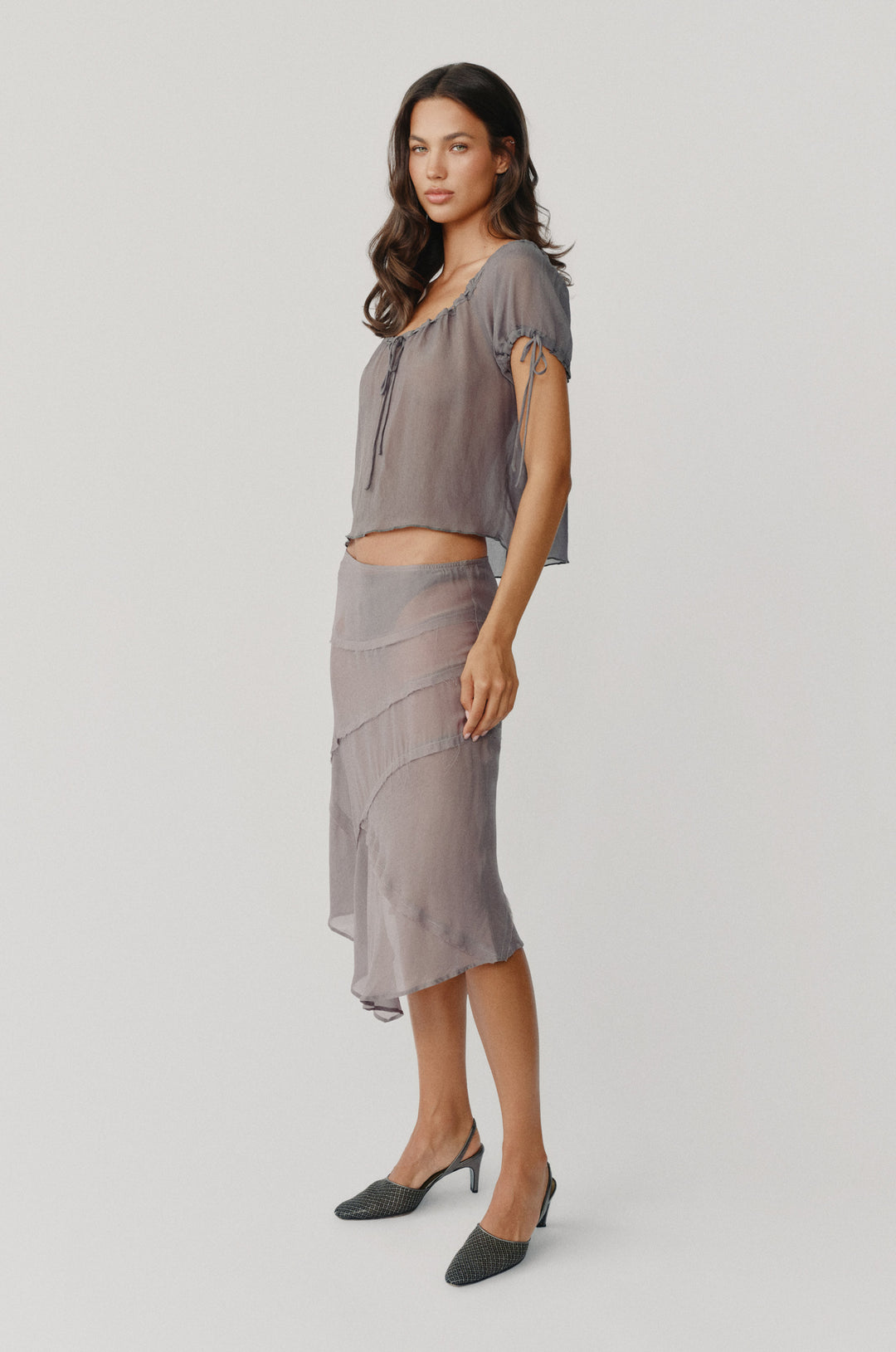Model wearing a sheer, dusty slate Gia skirt with frayed-edge panel detailing and an asymmetrical hem.