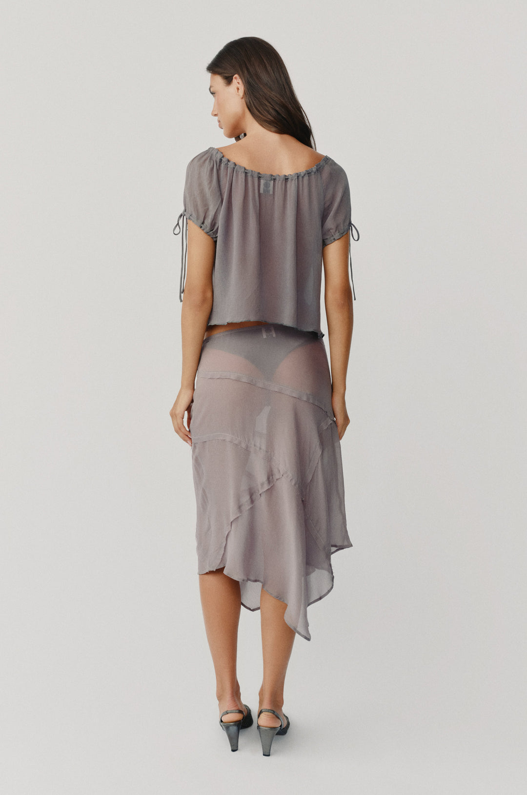 Ash slate sheer Gia top with adjustable neckline and tie-detail sleeves, paired with a matching asymmetrical sheer skirt.