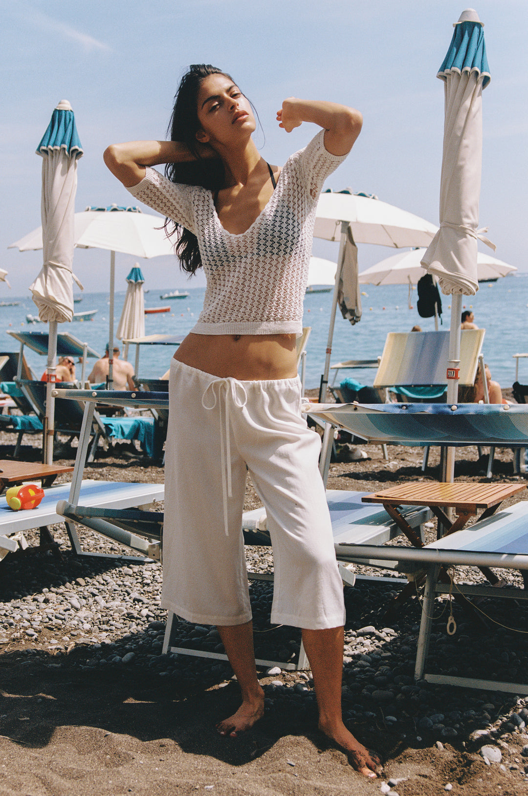 White Harper Top, knitted with scoop neckline, half sleeves, and contrast rib detailing, worn by a model on a beach.