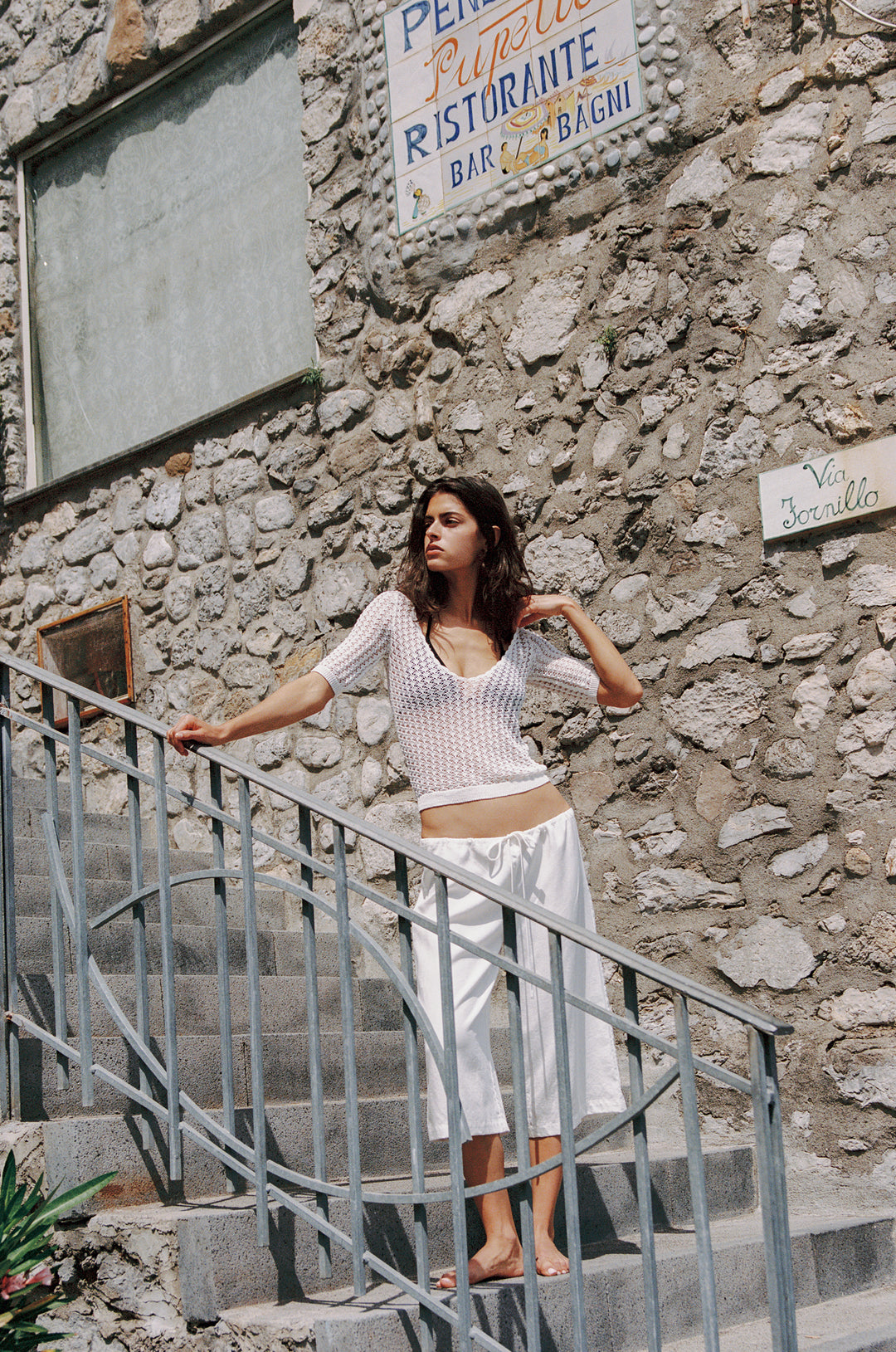 White Harper knitted top with scoop neck and half sleeves, paired with white pants, on stone steps.