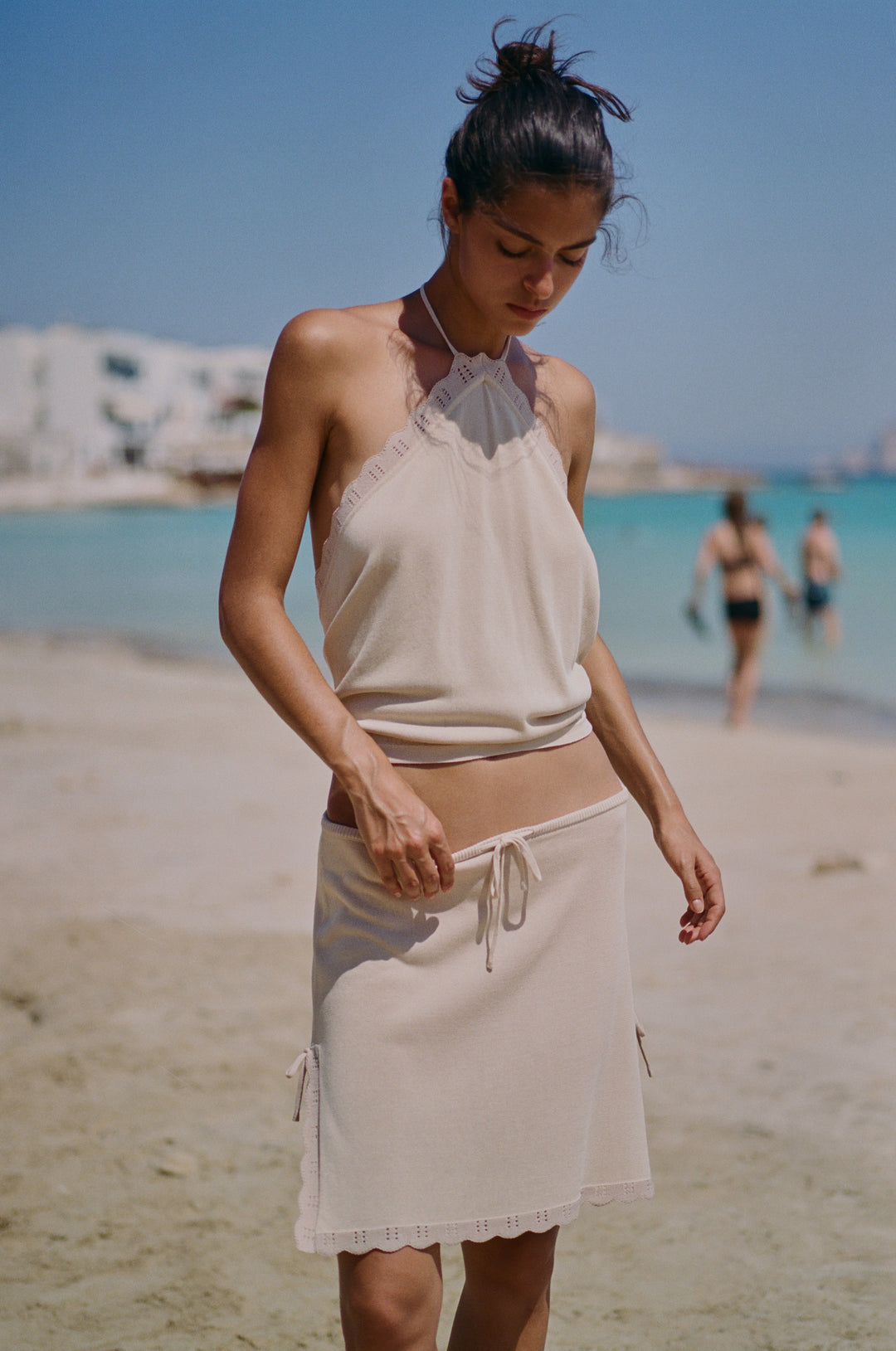 Beige low-rise Isla skirt with adjustable drawstring waist, scalloped trim, and side slits on a beach.