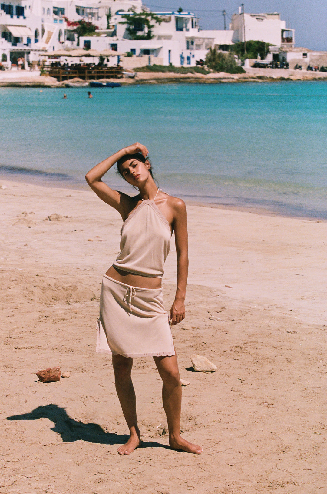 Beige low-rise Isla skirt with adjustable drawstring waist, scalloped trim, and side slits, worn on a sandy beach.