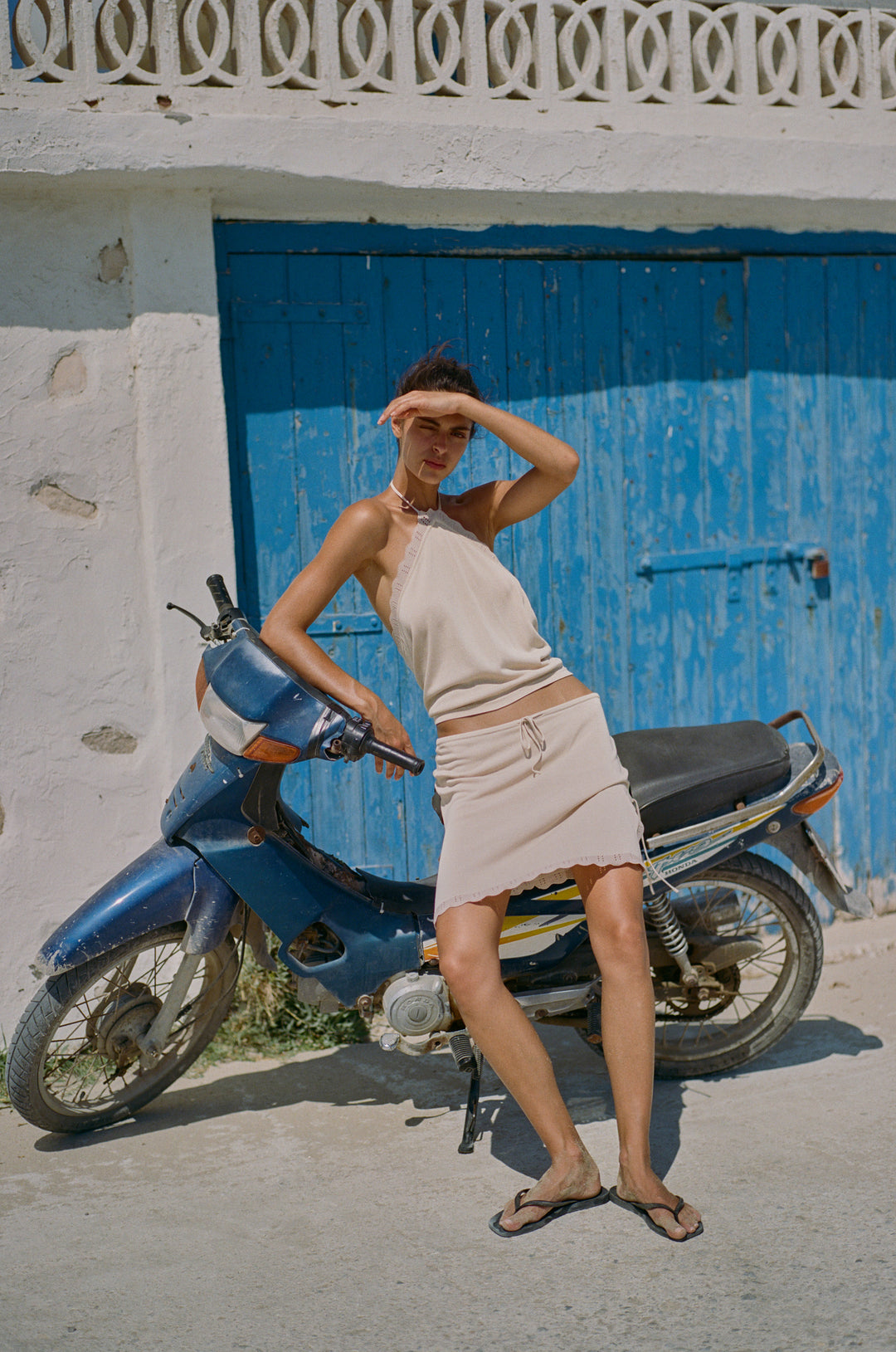 Beige knitted halter top with scalloped contrast trim and open back, styled with a matching mini skirt.