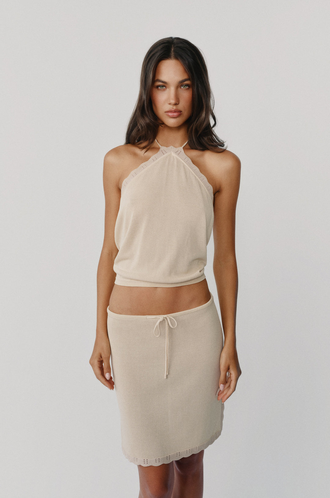 Beige knitted halter top with delicate scalloped contrast trim and a fitted hem worn with a matching skirt.