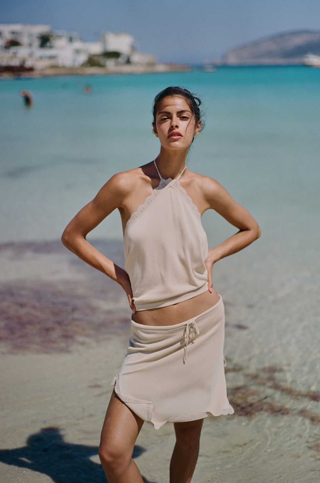 Beige knitted halter top with scalloped contrast trim and open back, worn on a beach.