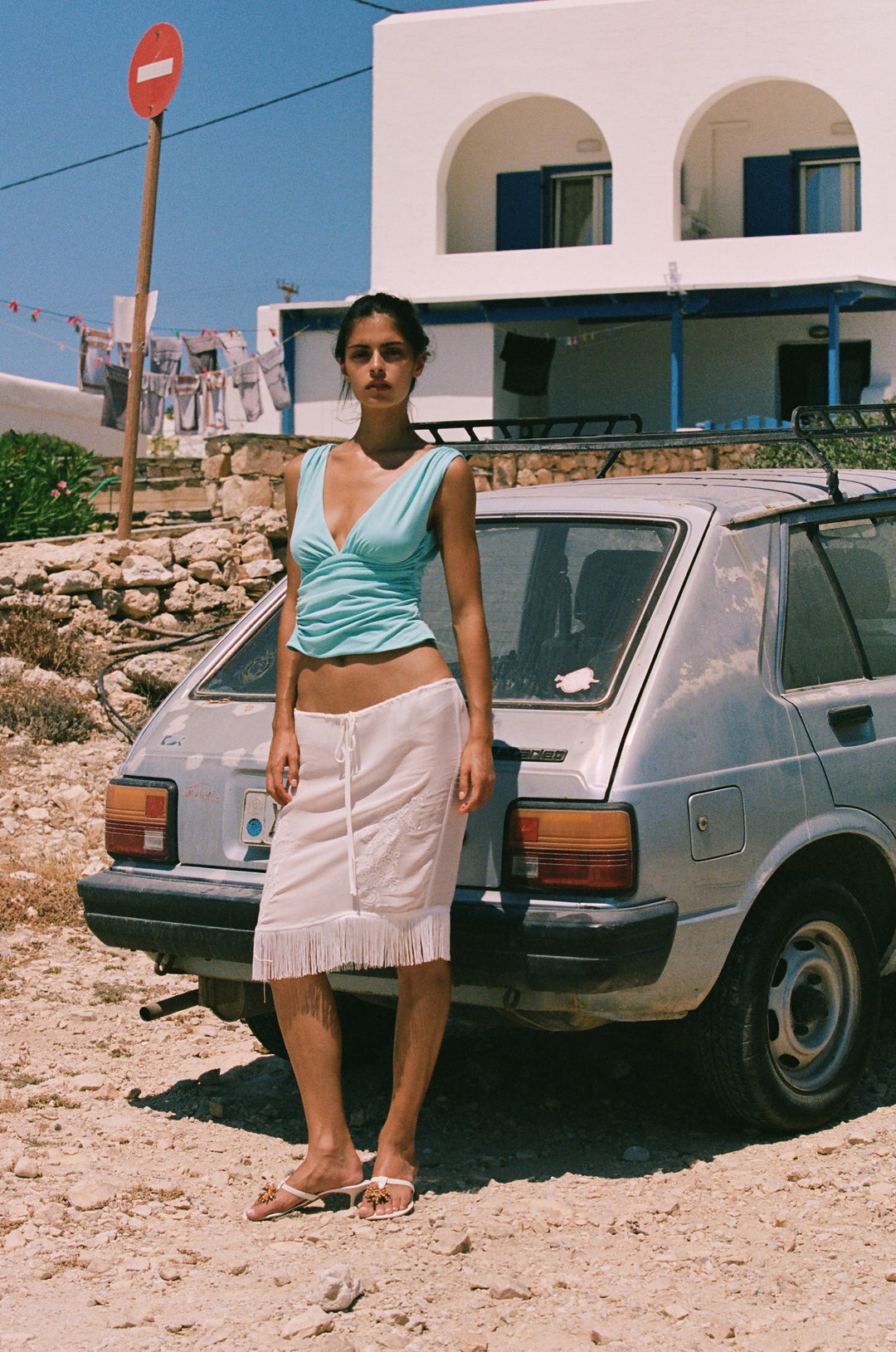 Sleeveless aqua Jane top with a V-neckline, gathered bust, and asymmetrical ruching, worn with a white fringe skirt.