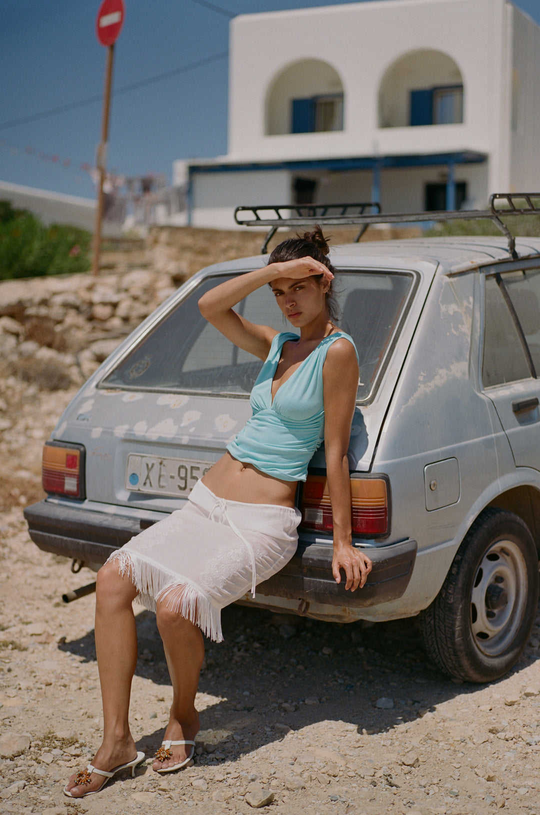 Sleeveless aqua Jane top with a V-neckline, gathered bust, and asymmetrical ruching, worn with a white fringe skirt.