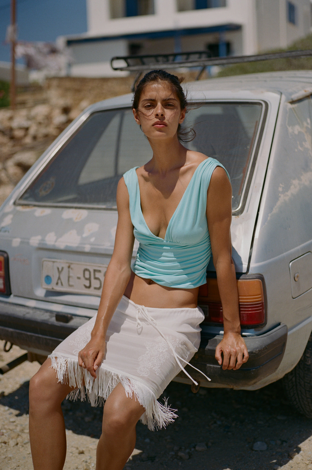 Sleeveless aqua Jane top with V-neck, gathered bust, and asymmetrical ruching, worn by a model leaning on a car.