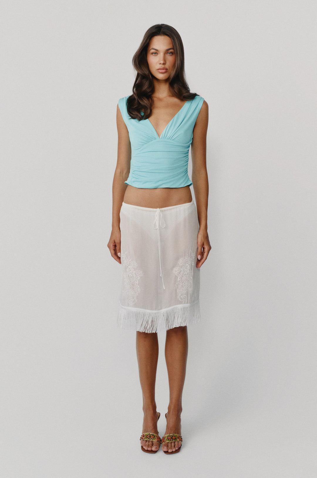 Sleeveless aqua Jane top with a V-neckline, gathered bust, and asymmetrical ruching, paired with a white skirt.