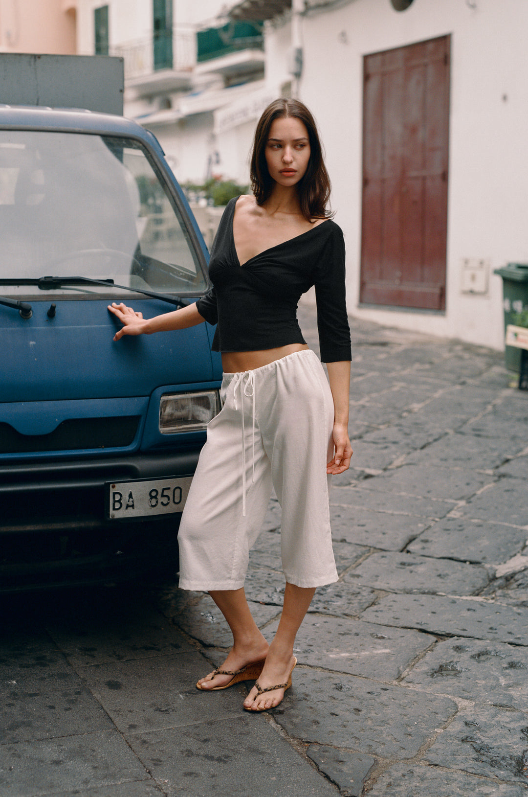 Woman in a black Lana V-neck top with half sleeves, gathered bust, and raw edge hems, posing by a blue van.