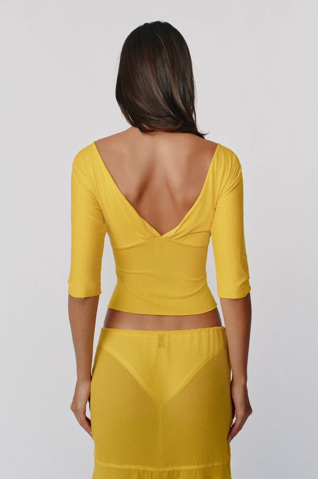 Golden yellow slim fit Lana top with half sleeves and a deep V-back, paired with a matching sheer skirt.