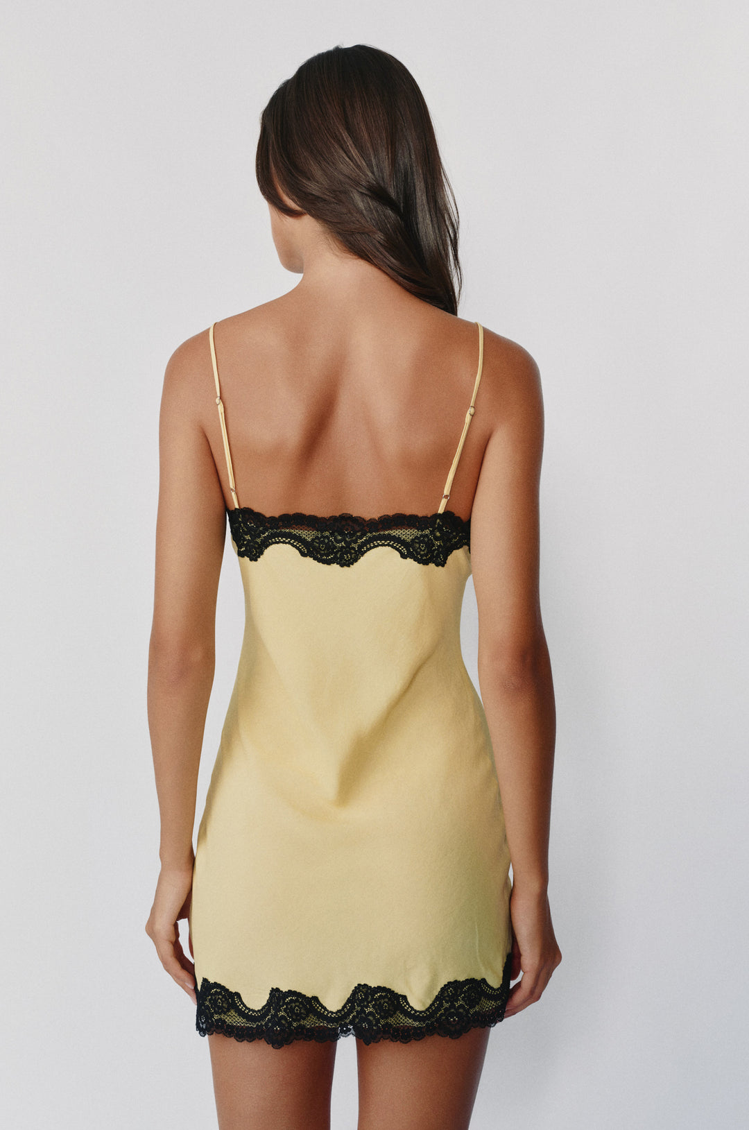 Pale yellow mini slip dress with adjustable straps and black lace trim on the neckline and hem.