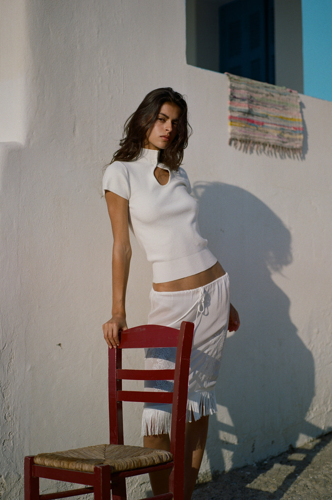 White knitted short-sleeve top with a high neck, button closure, and front keyhole cutout, worn with a white skirt.