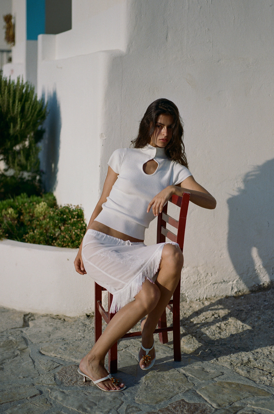 White knitted short-sleeve top featuring a high neck, button closure, and front keyhole cutout, worn with a white skirt.