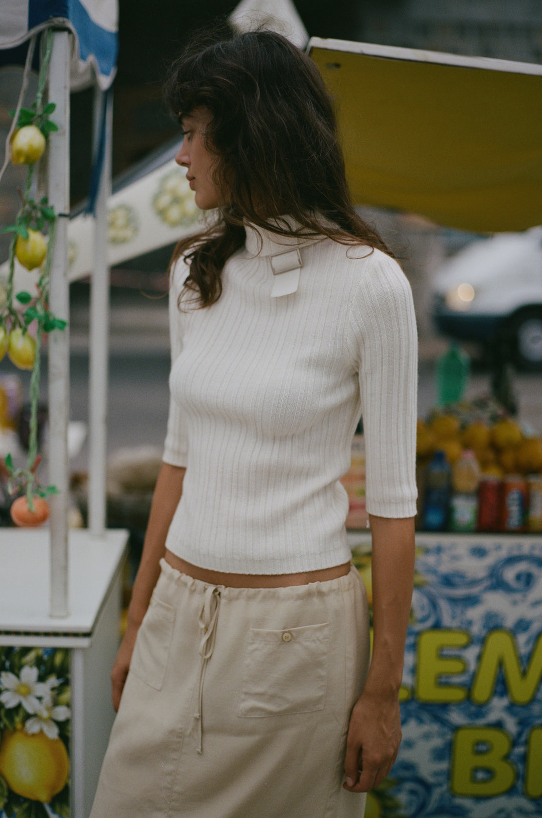 Off-white fine wool-knit top with a high neckline, adjustable buckle detail, and half sleeves.