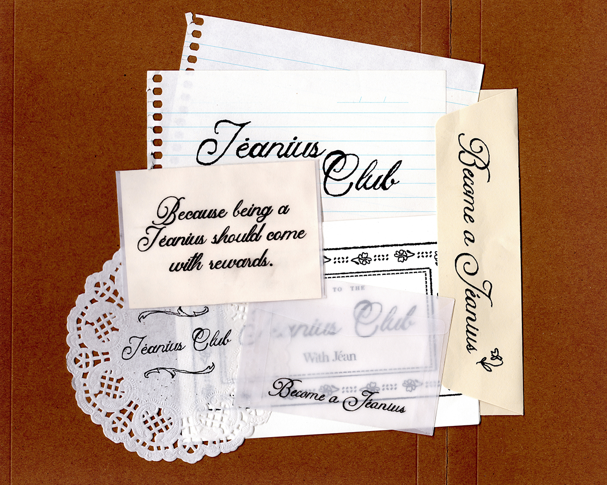 A flat-lay arrangement of vintage-style paper ephemera and stationery items on a brown textured background, including a lined notepad, cream cards with black script text reading 'Jeanius Club' and 'Become a Jeanius', a white lace doily, and a clear plastic sleeve. desktop
