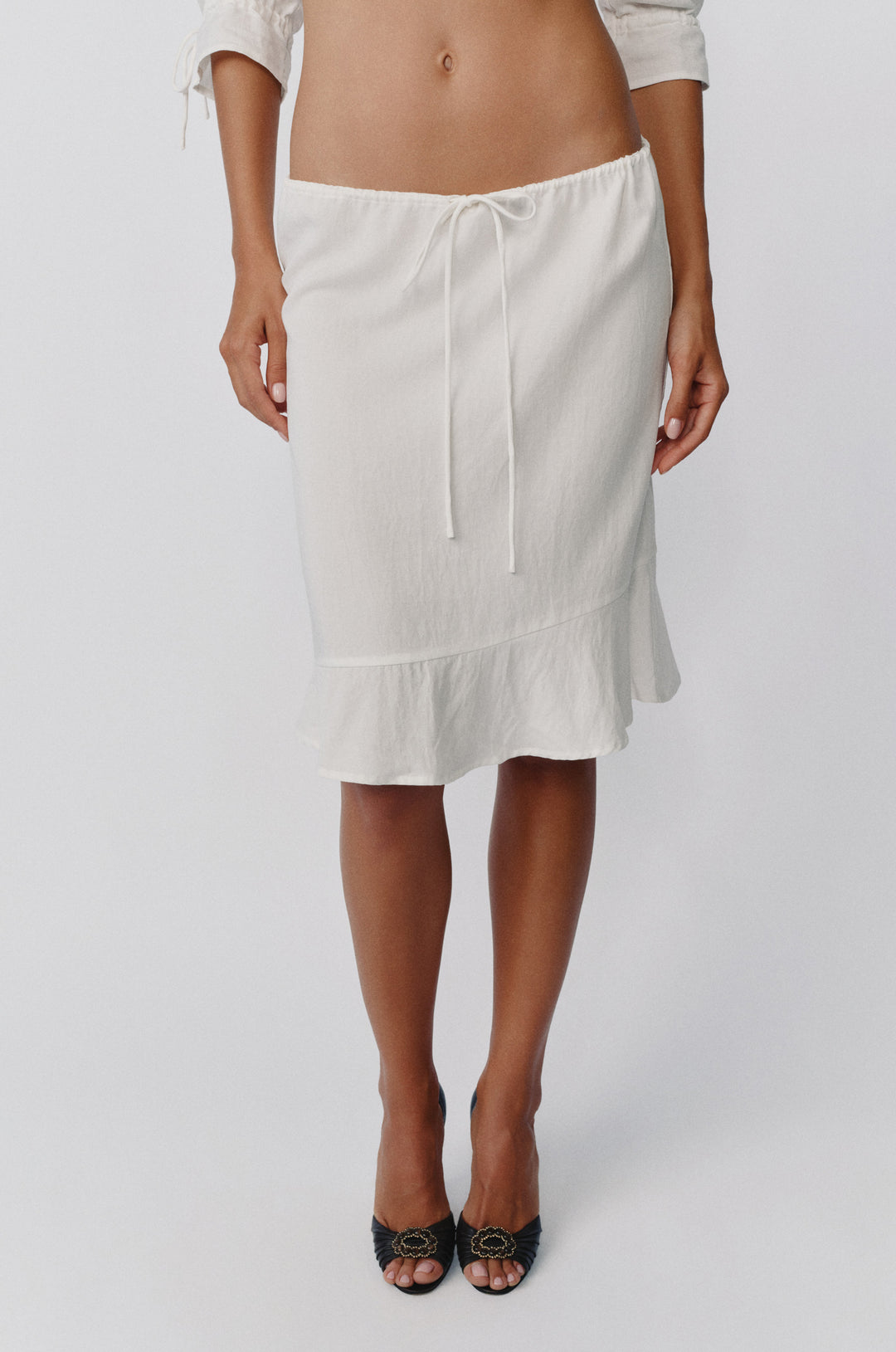 White low-rise Maisie skirt with an adjustable drawstring waist and asymmetrical ruffle hem detail.