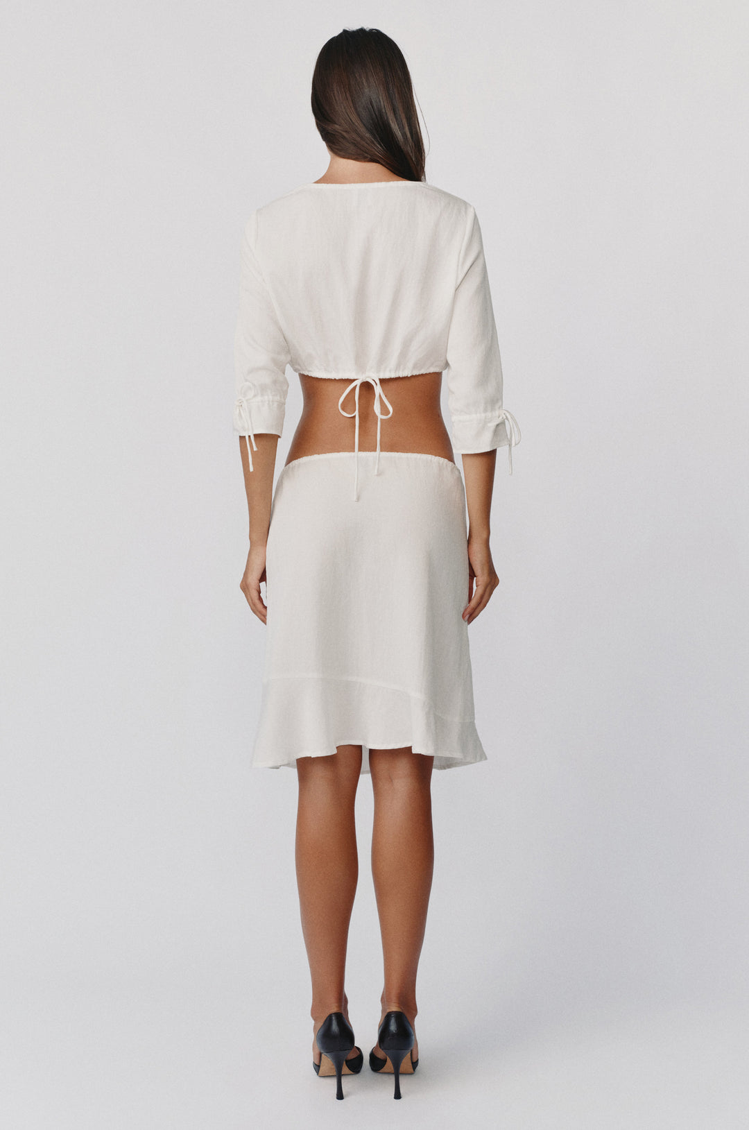 White low-rise Maisie skirt with an adjustable drawstring waist and asymmetrical ruffle hem, worn from the back.