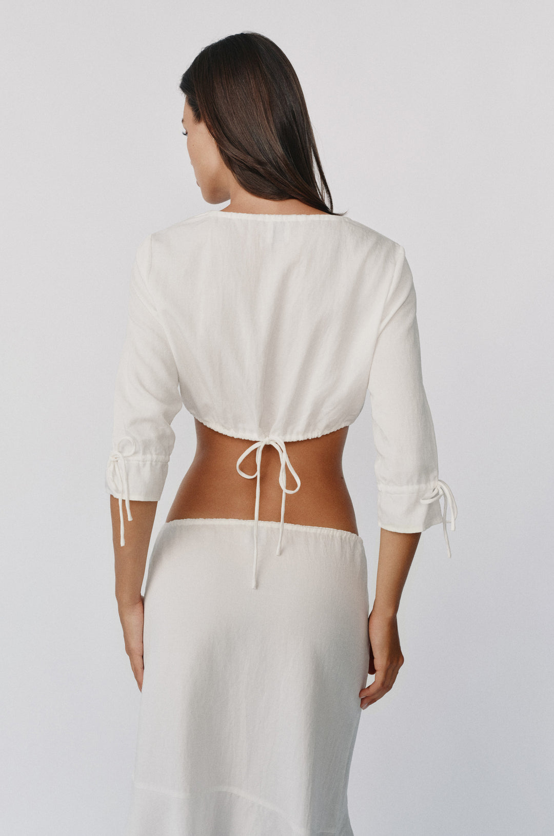 White cropped Maisie top with 3/4 sleeves, ruffle cuffs, and an adjustable drawstring tie hem worn from the back.