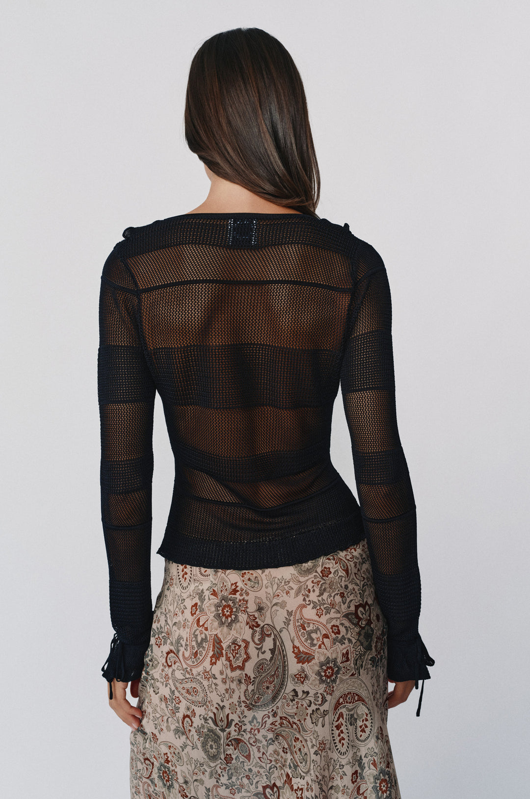 Back view of a black long-sleeve knitted top with sheer striped texture and tie detailing on the cuffs.