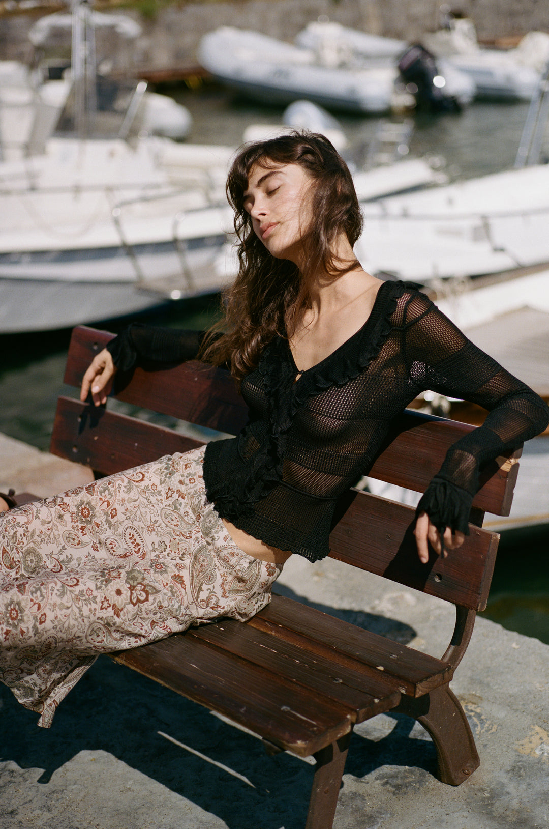 Black knitted long-sleeve top with a ruffle-trimmed button neckline and tie-detail cuffs worn with a patterned skirt.