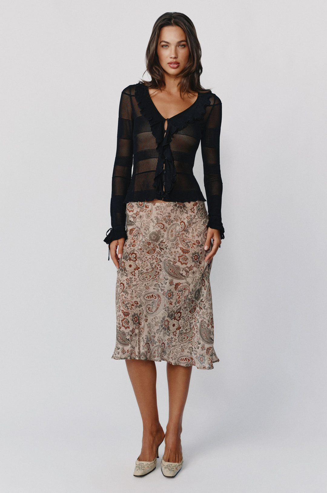 Black knitted Malia top with long sleeves, ruffle trim, button-front neckline, and tie-detail cuffs worn with a paisley skirt.