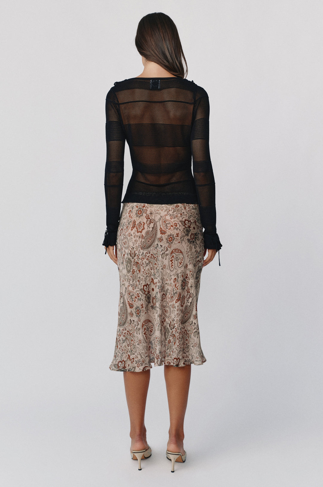 Back view of a black long-sleeve knitted Malia top with tie cuffs, paired with a patterned paisley midi skirt.
