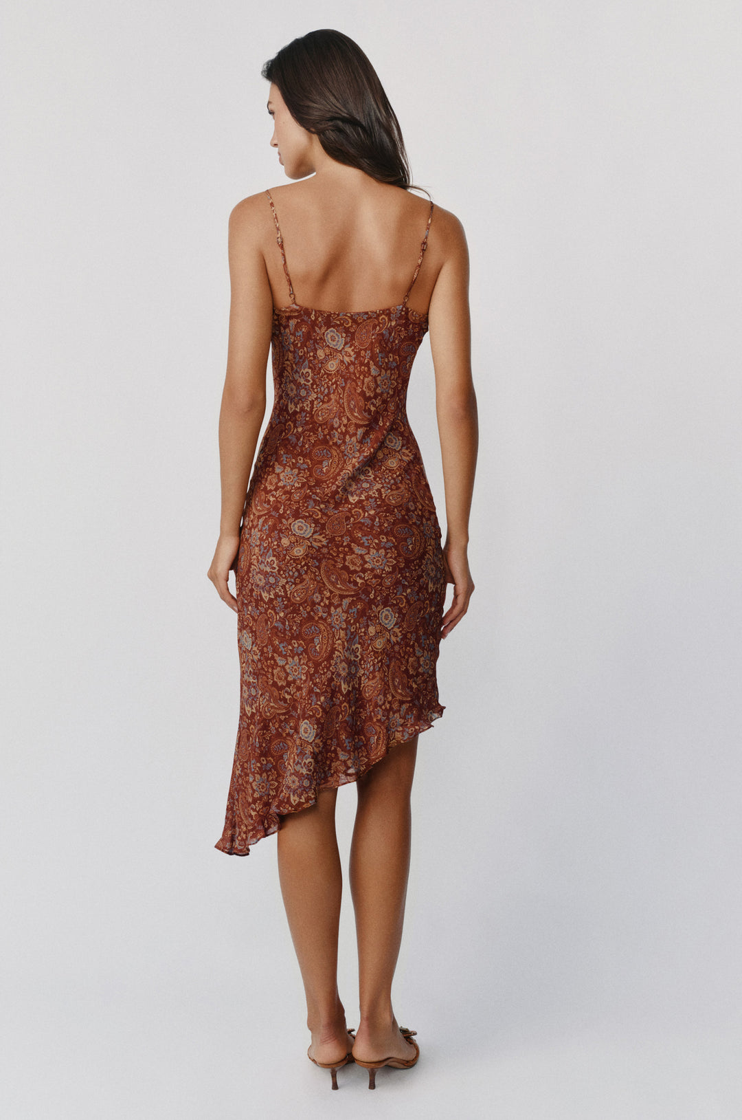 Back view of the Mallory dress in terra paisley print, featuring thin spaghetti straps and an asymmetrical midi hemline.