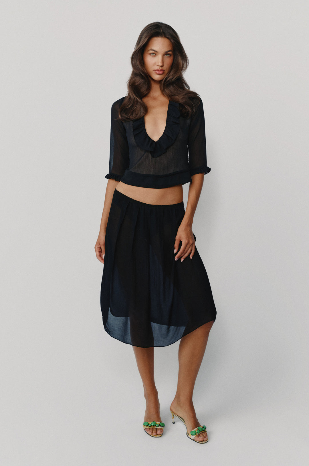 Black Nadia blouse with deep V-neck, ruffle trim, and 3/4 sleeves, paired with a matching sheer midi skirt.