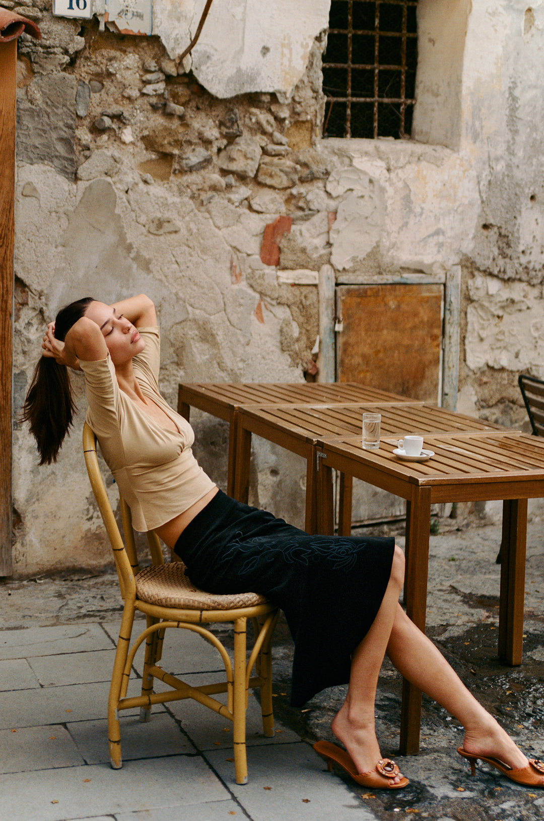 Black Naomi midi skirt with custom embroidered floral applique and front slit, worn by a woman sitting outdoors.