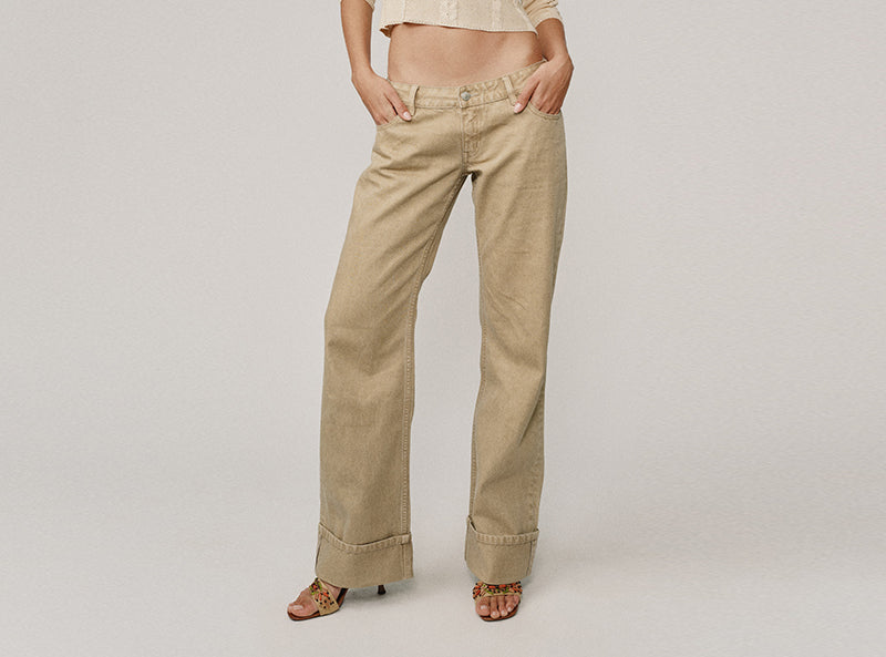 A model wearing beige wide-leg cropped jeans with rolled cuffs, paired with a matching beige crop top and brown sandals, photographed against a neutral light gray studio background.