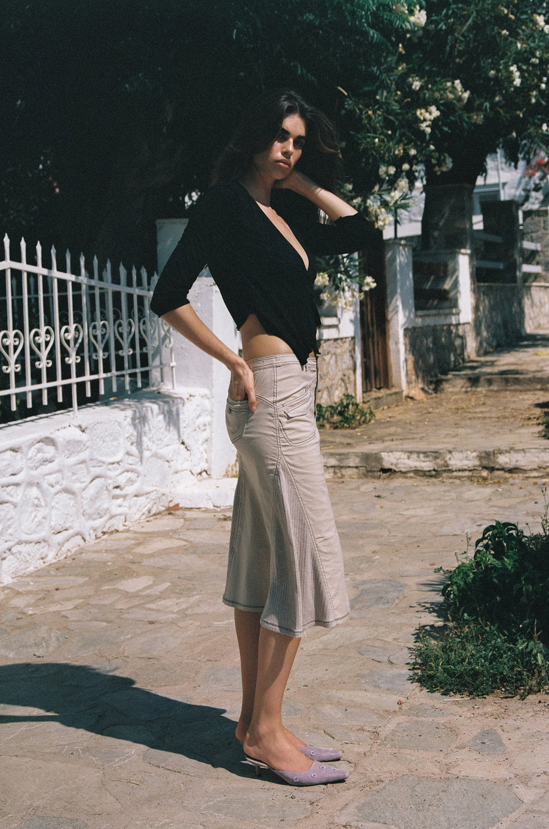 Black wrap-style Nelly top with 3/4 sleeves, V-neck, and ruffle detail, worn with a beige midi skirt outdoors.