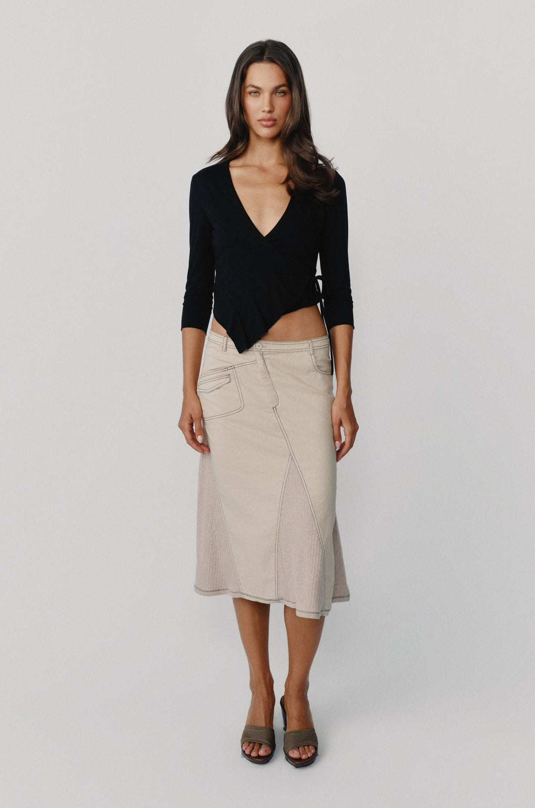Black wrap-style Nelly top with V-neckline, 3/4 sleeves, and asymmetrical hem paired with a beige midi skirt.