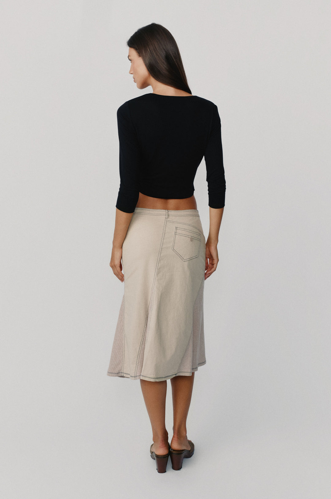 Model wearing a black Nelly wrap top with 3/4 sleeves paired with a beige midi skirt.