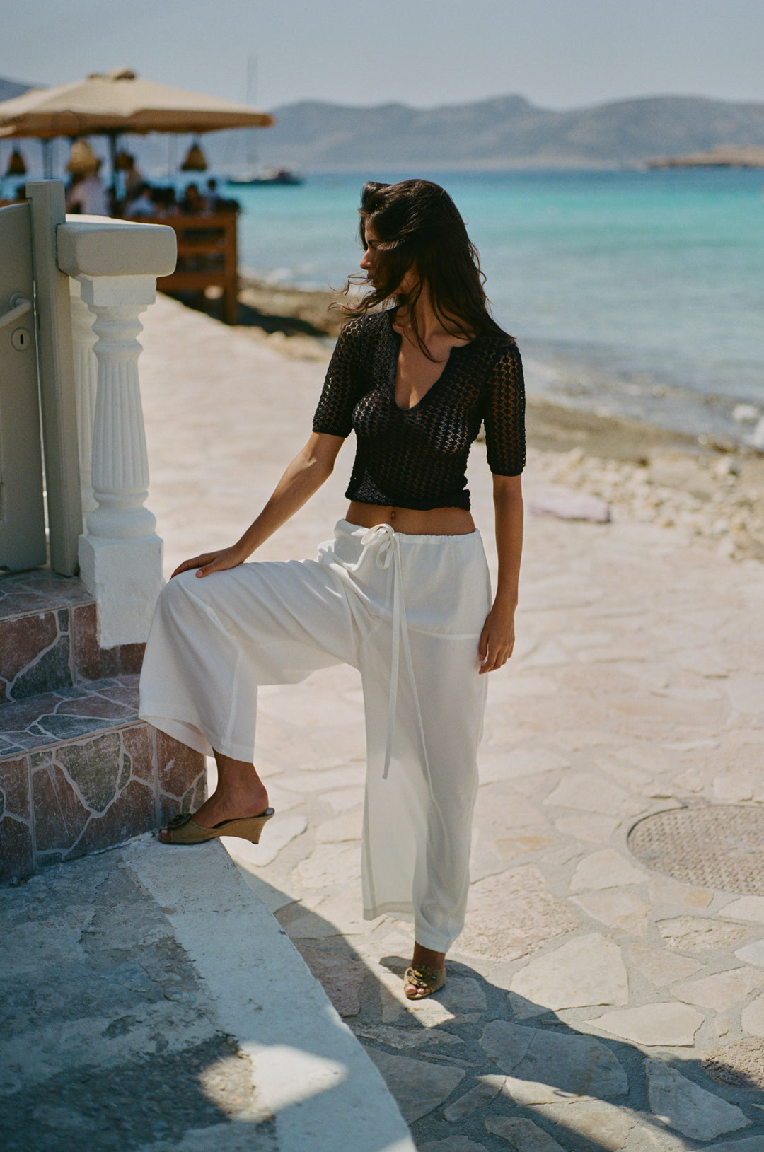 Woman wearing loose-fit white Norah pants with a self-fabricated tie waistband, styled with a black crochet top.