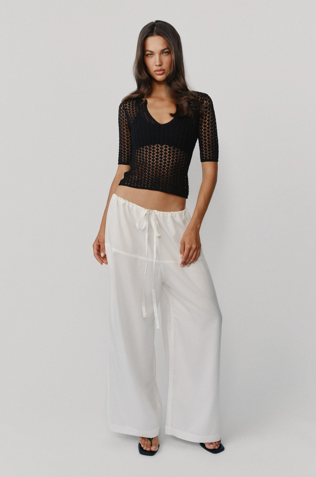 Model wearing loose-fit white Norah pants with a drawstring waistband and a black crochet top.
