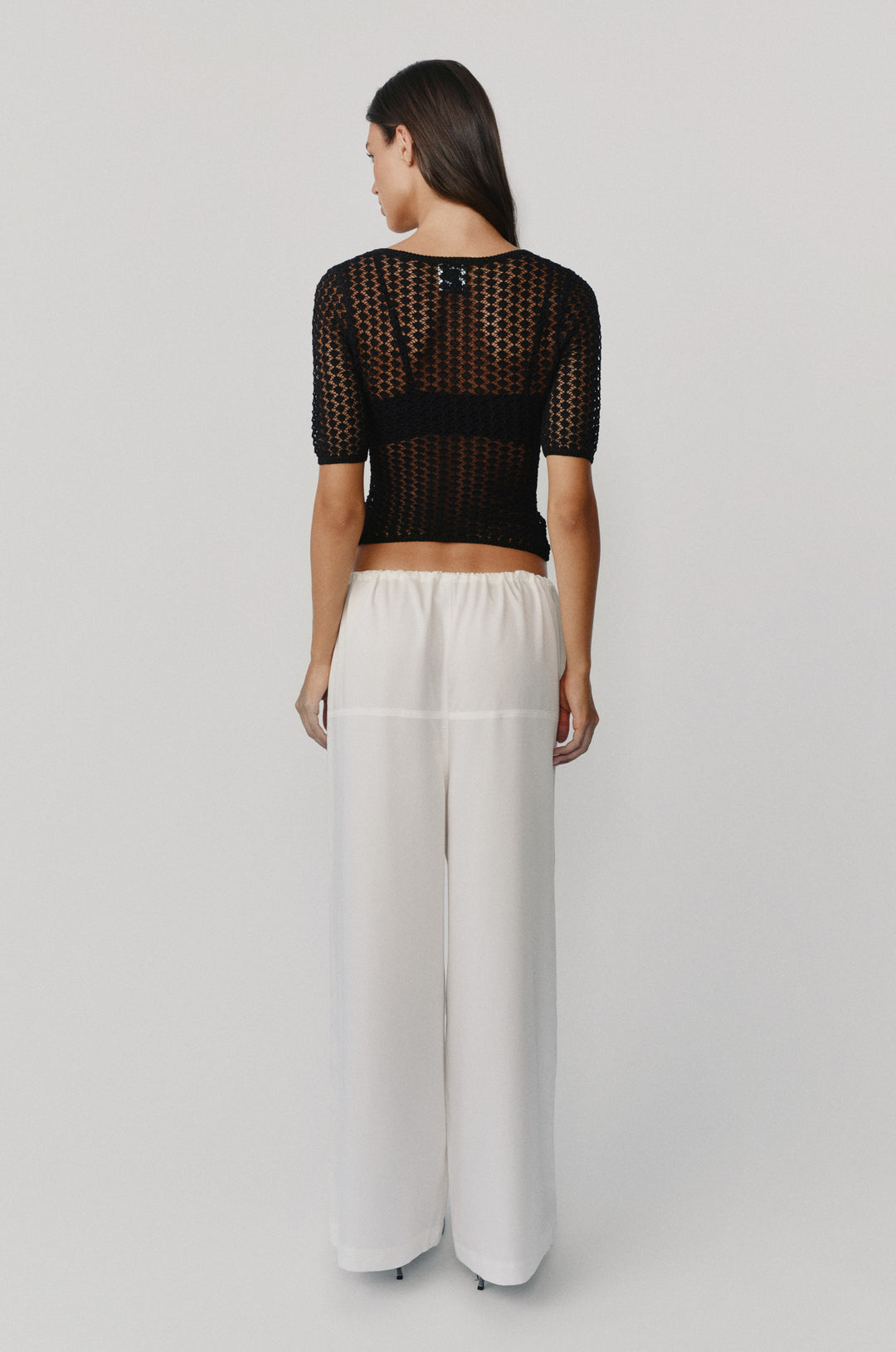 Back view of white Norah loose-fit pants with a comfortable elasticated waistband, paired with a black crochet top.