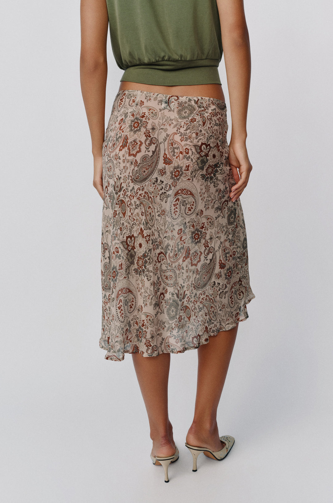 Olea midi skirt in stone paisley print with a sheer finish, styled low on the hips with a green top and heeled mules.