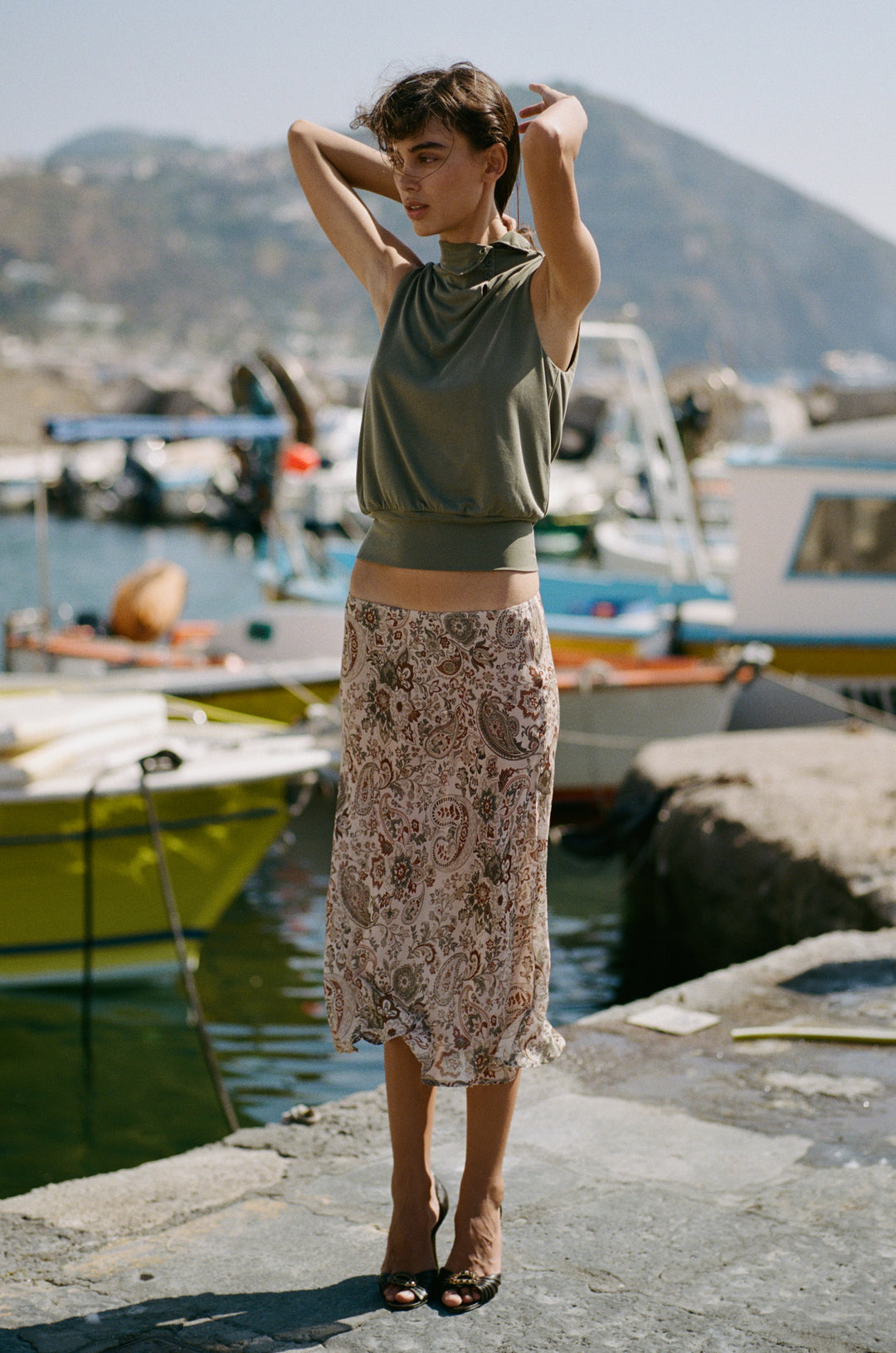 Olea skirt in stone paisley print with a sheer finish, worn low on the hips by a woman standing on a harbor dock.