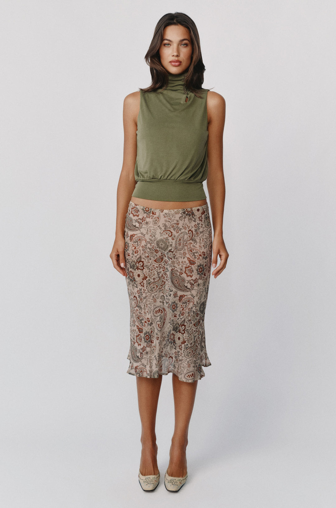 Model wearing a sheer, low-rise Olea midi skirt in a stone paisley print paired with an olive green sleeveless top.