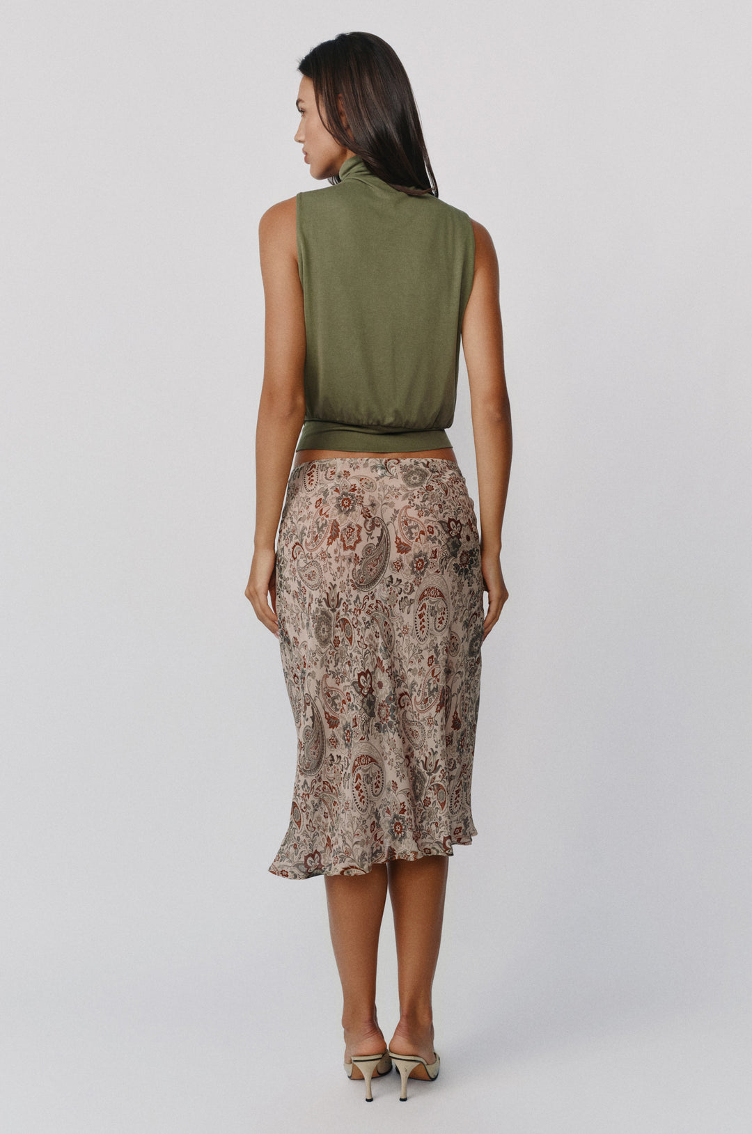 Model wearing a sheer, low-rise Olea midi skirt in a stone paisley print paired with an olive green sleeveless top.