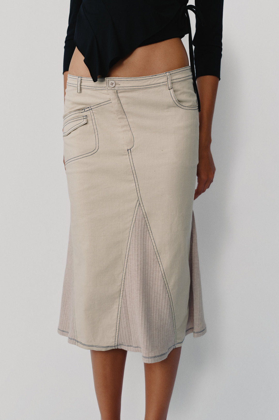 Taupe low-rise midi skirt with asymmetric pockets, contrast topstitching, and ribbed panel detailing.