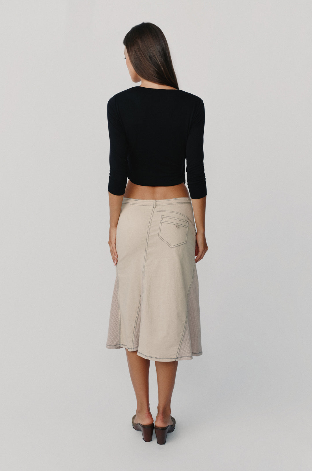 Taupe low-rise midi skirt with asymmetric back pockets, contrast topstitching, and ribbed side panels worn with a black top.