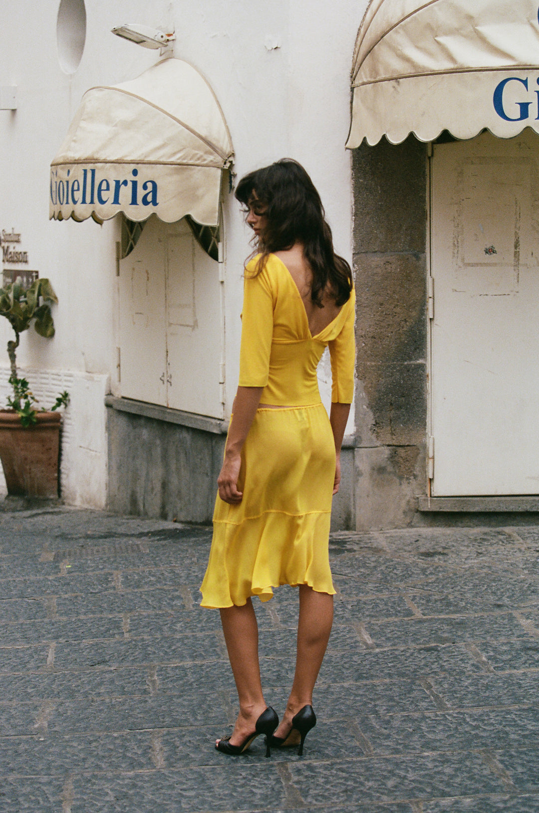 Model wearing a sheer, golden yellow Pali skirt with an adjustable drawstring waist and flowy drop-seam hemline.