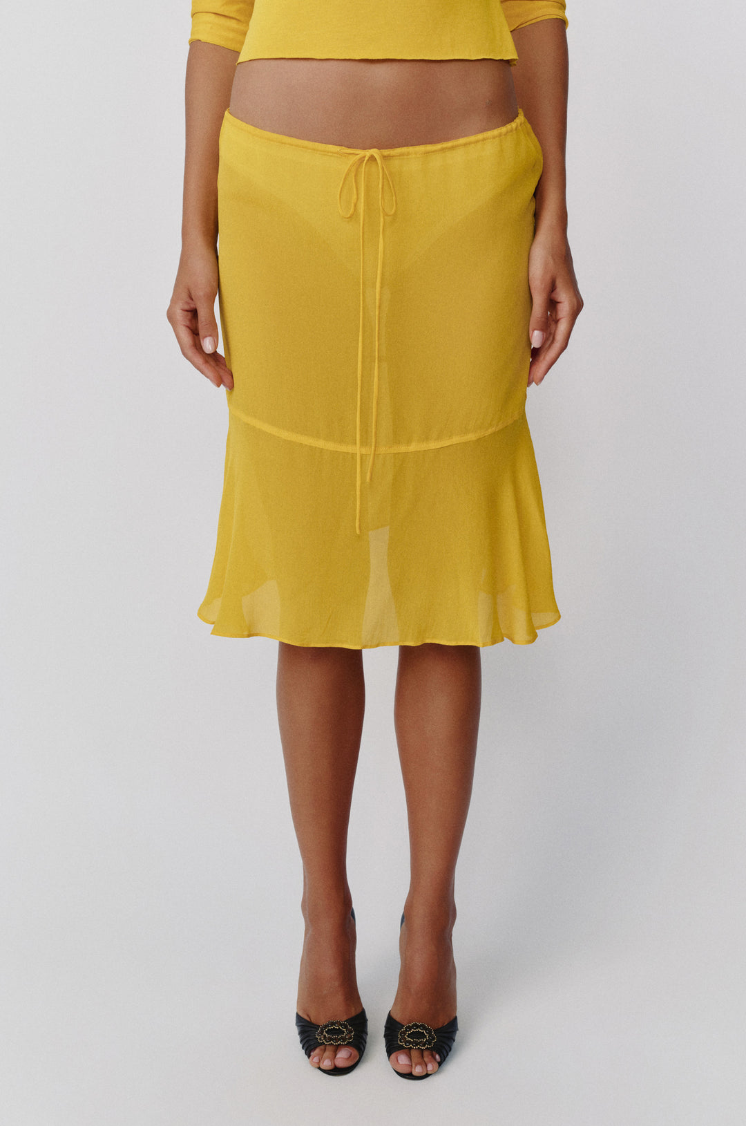 Sheer golden yellow low-rise Pali skirt with an adjustable drawstring waist and a flowy drop-seam curved hem.