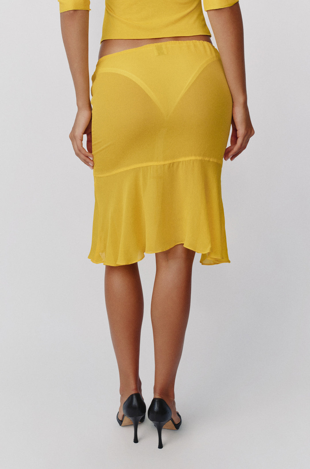 Golden yellow sheer low-rise Pali skirt with an adjustable drawstring waist and a flowy, curved drop-seam hemline.