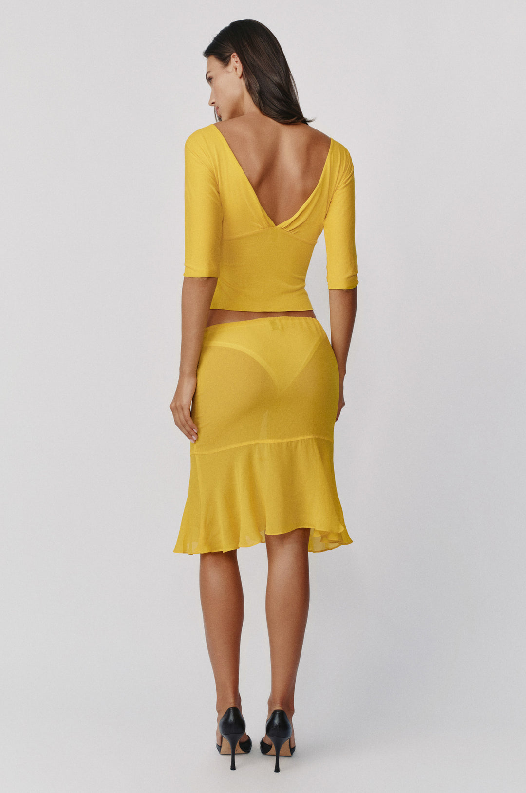 Golden yellow sheer Pali skirt with a low-rise drawstring waist and a flowy drop seam hemline worn with a matching top.