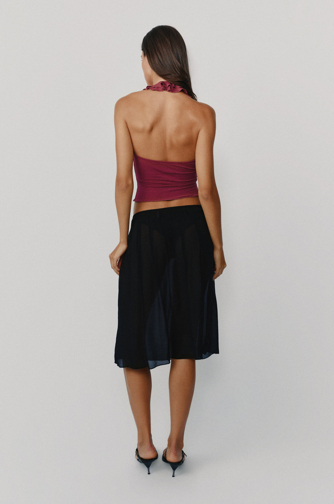 Plum Ruby halter top with ruffle-trim neckline and open back, paired with a sheer black midi skirt.