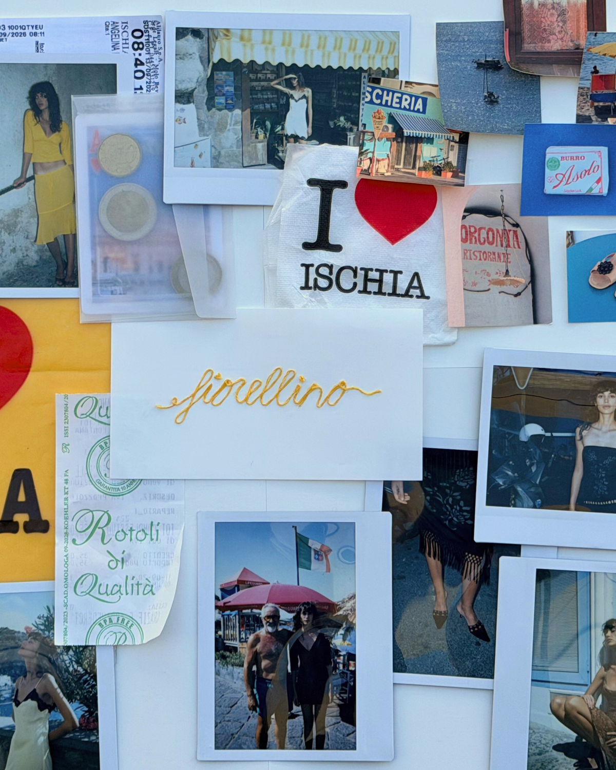 A collage of travel photographs, postcards, and printed cards pinned or taped to a white board. Prominent items include a white card reading 'I ♥ ISCHIA' with a red heart, a gold script card reading 'sinellino', a green circular card reading 'Rotoli di Qualita', and several fashion and street-scene photos.