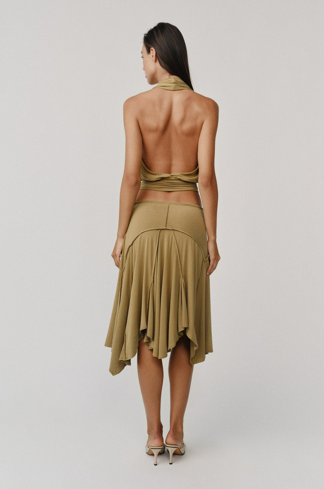 Woman from behind wearing an olive midi-length Sharni Skirt with an adjustable tie waistband and draped hem.